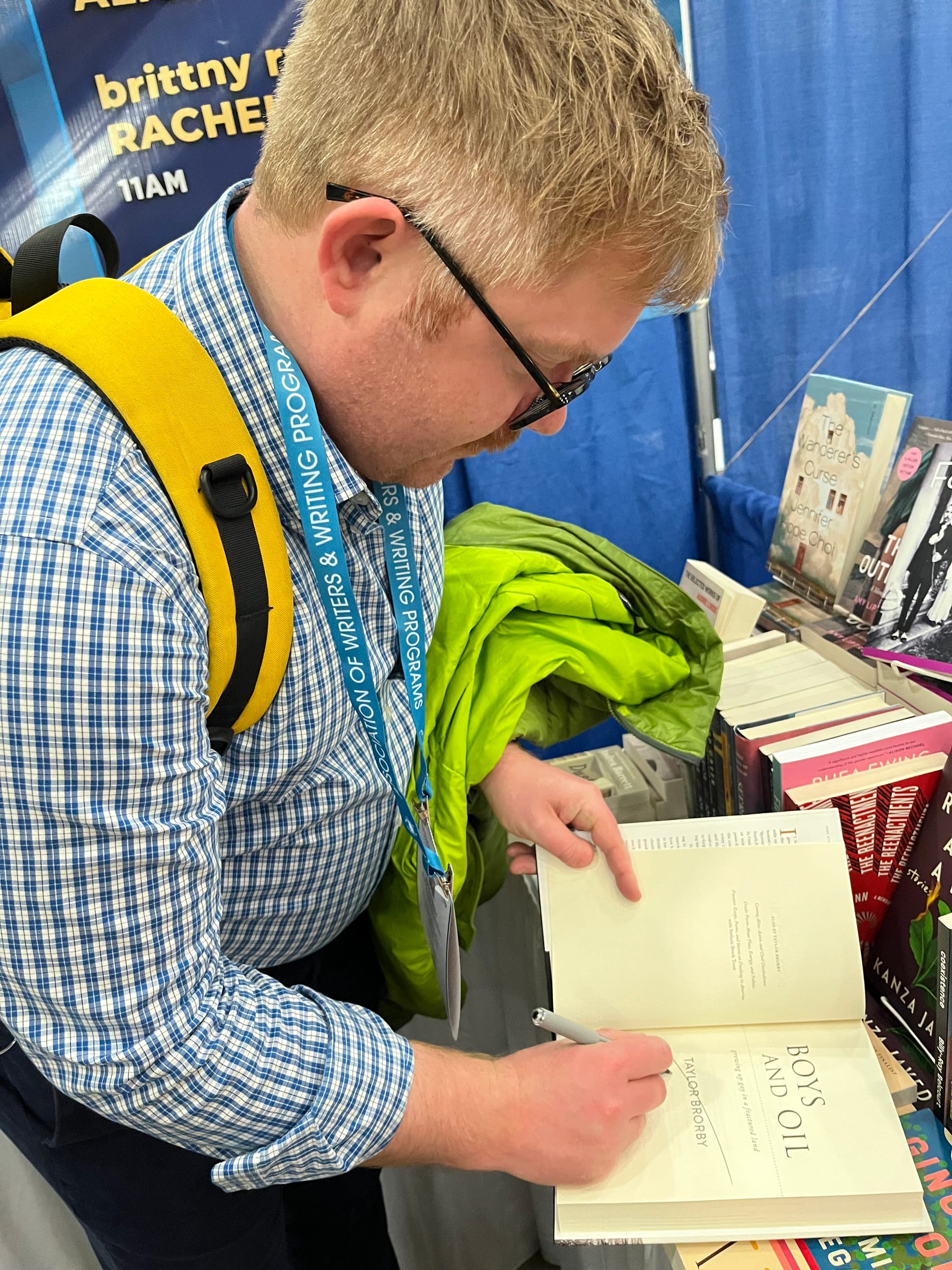 Author Taylor Brorby signing his book at a table with other books from different authors.