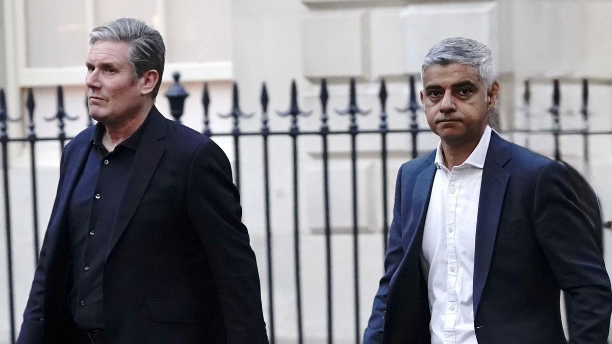 Kier Starmer walks on the street in a dark shirt and black jacket next to Sadiq Khan who wears a white shirt and navy blue jacket