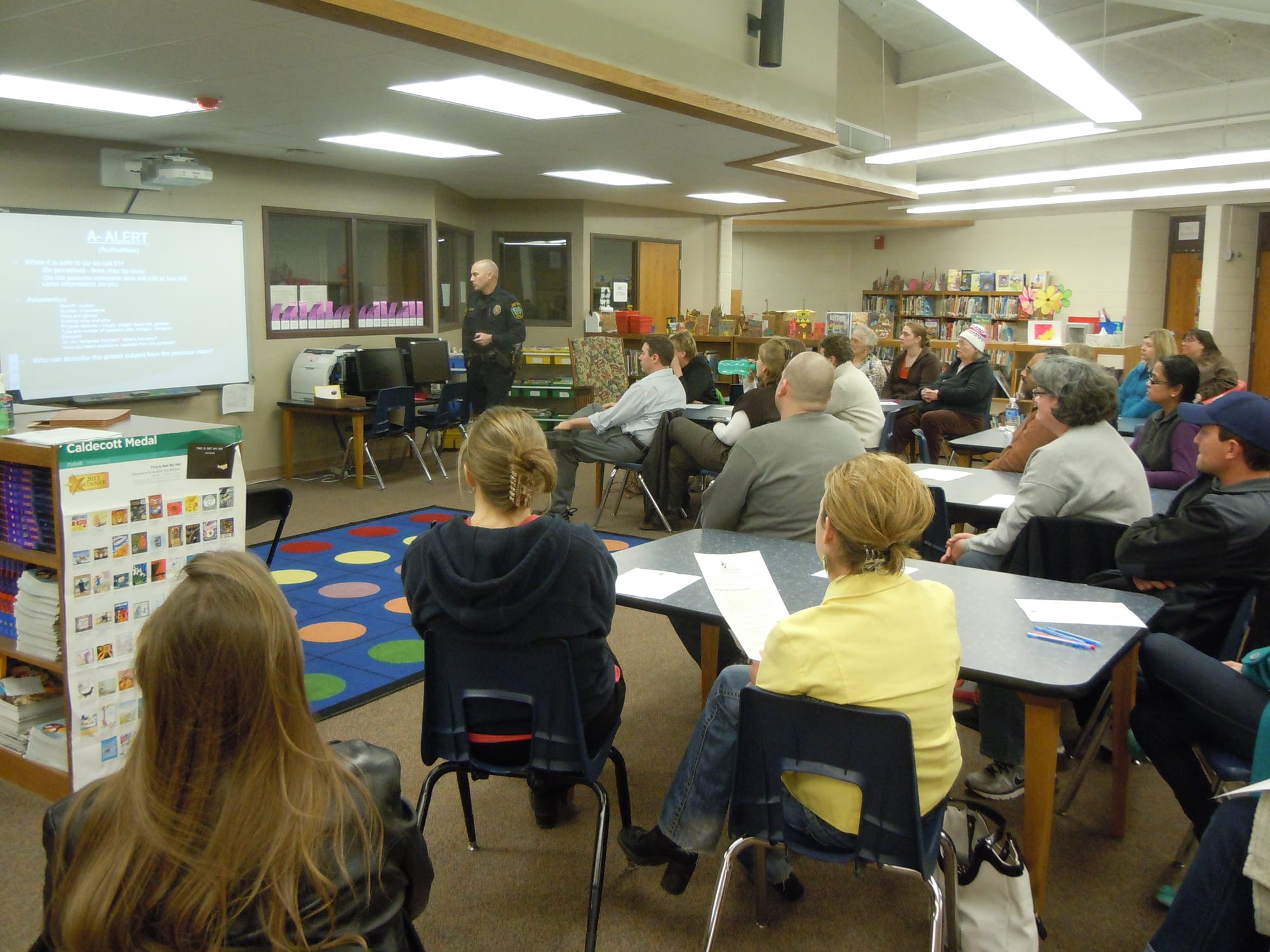 Parents listen while Iowa City Police Officer Derek Frank presents information on ALICE during an informational meeting.