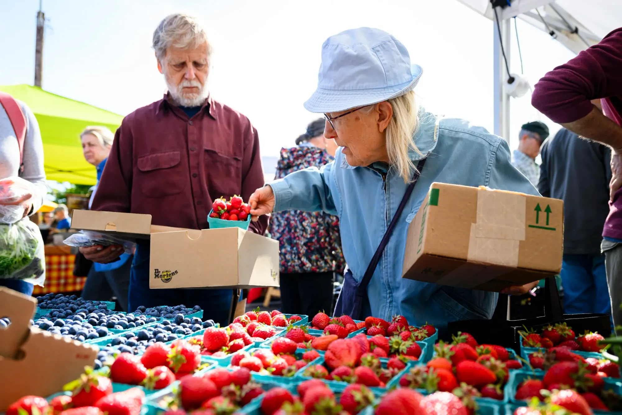 Judy Dobkevich hands fresh strawberries to her husband, Michael Dobkevich, at the Port Townsend Farmers Market. The Dobkevichs use food access programs to help supply their pantry with fresh fruit and vegetables. Photo by Heather Johnson