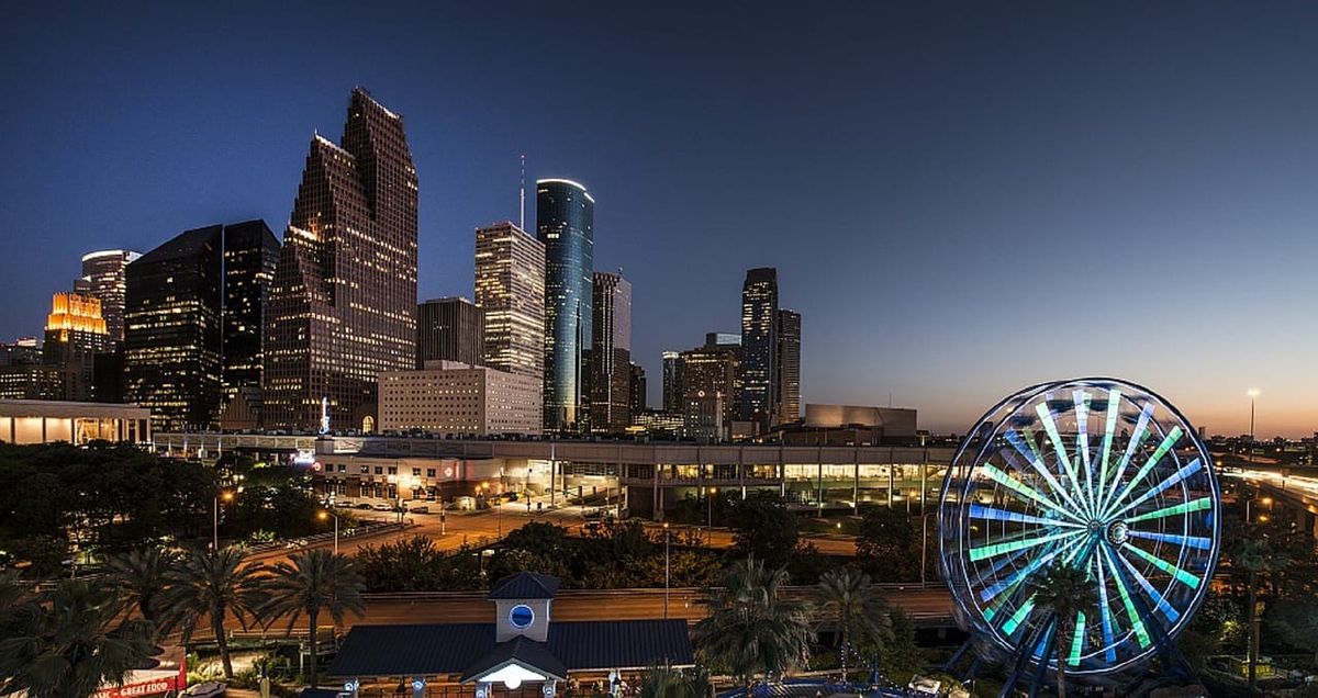 Houston skyline at dusk with illuminated skyscrapers and a glowing Ferris wheel in view.