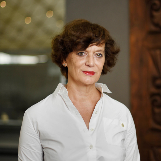 Portrait of Souraya Noujaim, newly appointed director of Louvre Abu Dhabi, wearing a white shirt against a neutral background.
