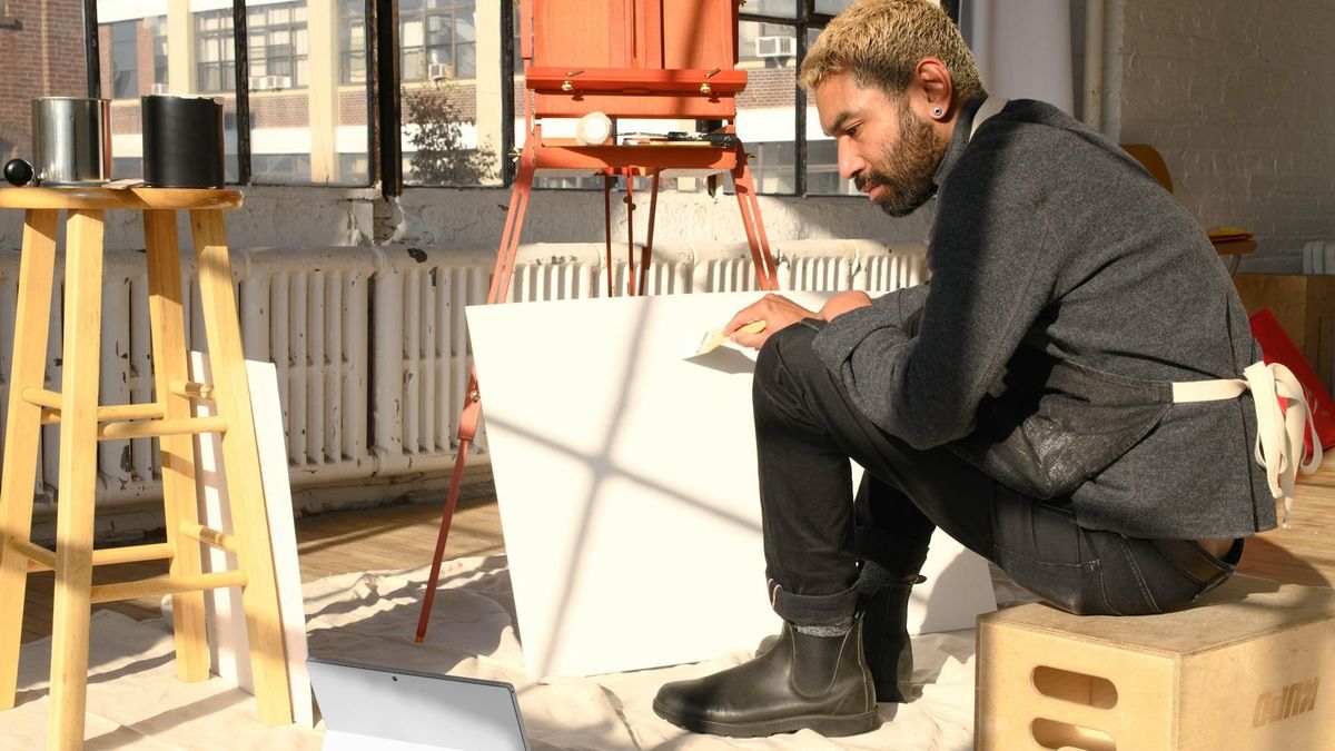 Art student with multiple test paintings in a studio, suggesting experimentation, public feedback, and early support for developing work.