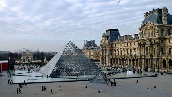 Visitors lining up beneath the Louvre pyramid on a cold day in Paris.