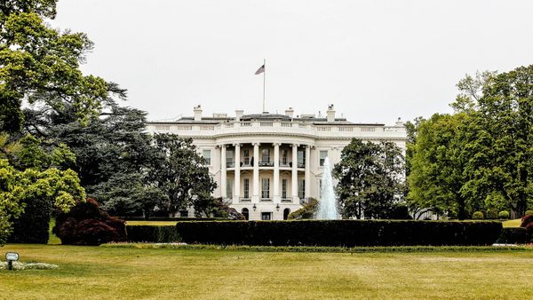 The White House seen in daylight, framed by green lawns and clear skies.
