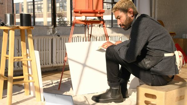 Art student with multiple test paintings in a studio, suggesting experimentation, public feedback, and early support for developing work.