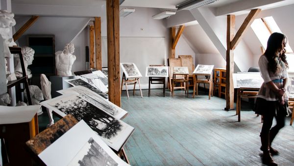 Graduating art student walking out of a school studio carrying portfolio materials, suggesting the beginning of a sustainable artistic practice.