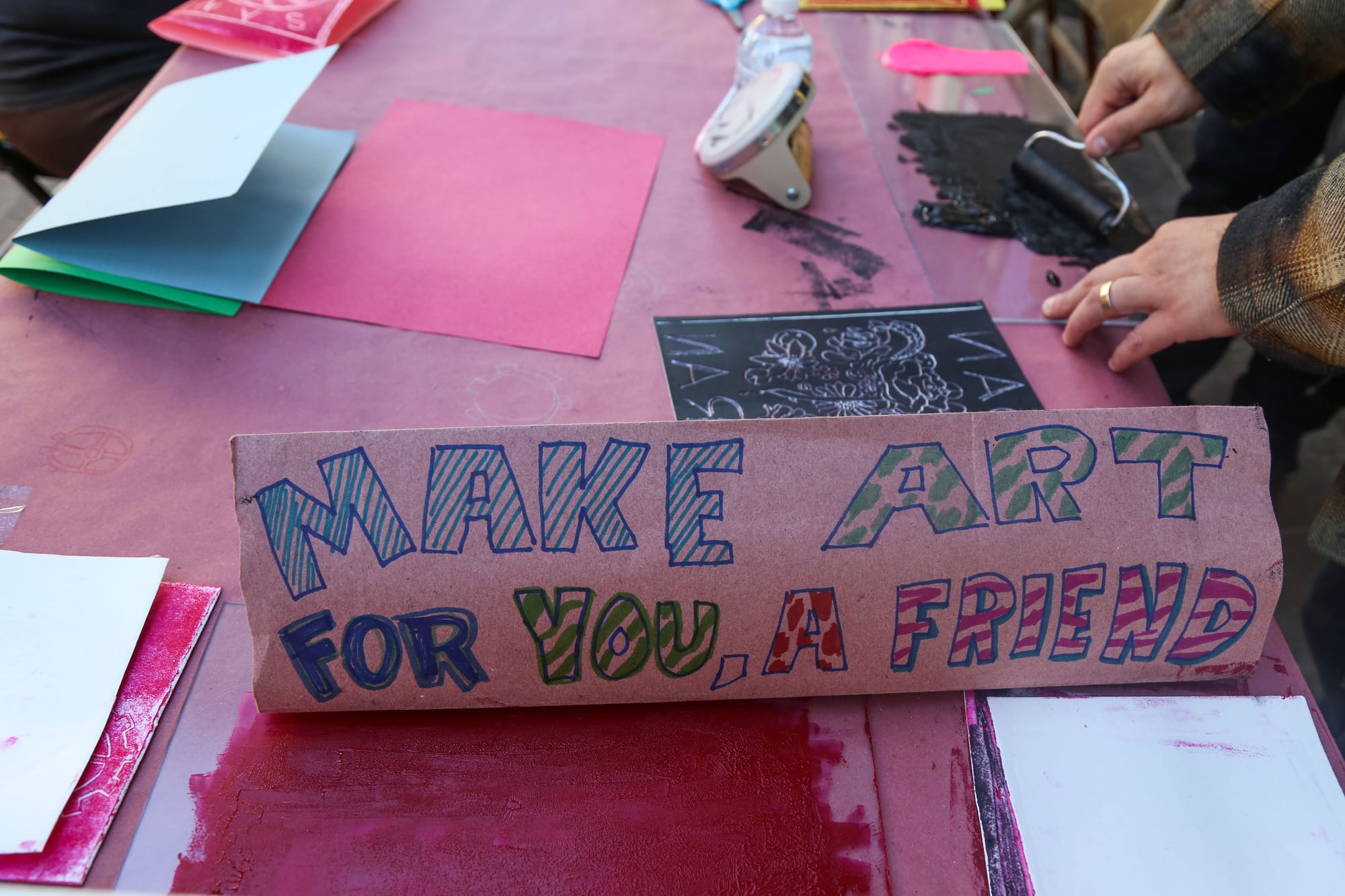 A sign reading “Make art for you, a friend,” rests on the table inviting people in downtown San Francisco to sit and create artwork.