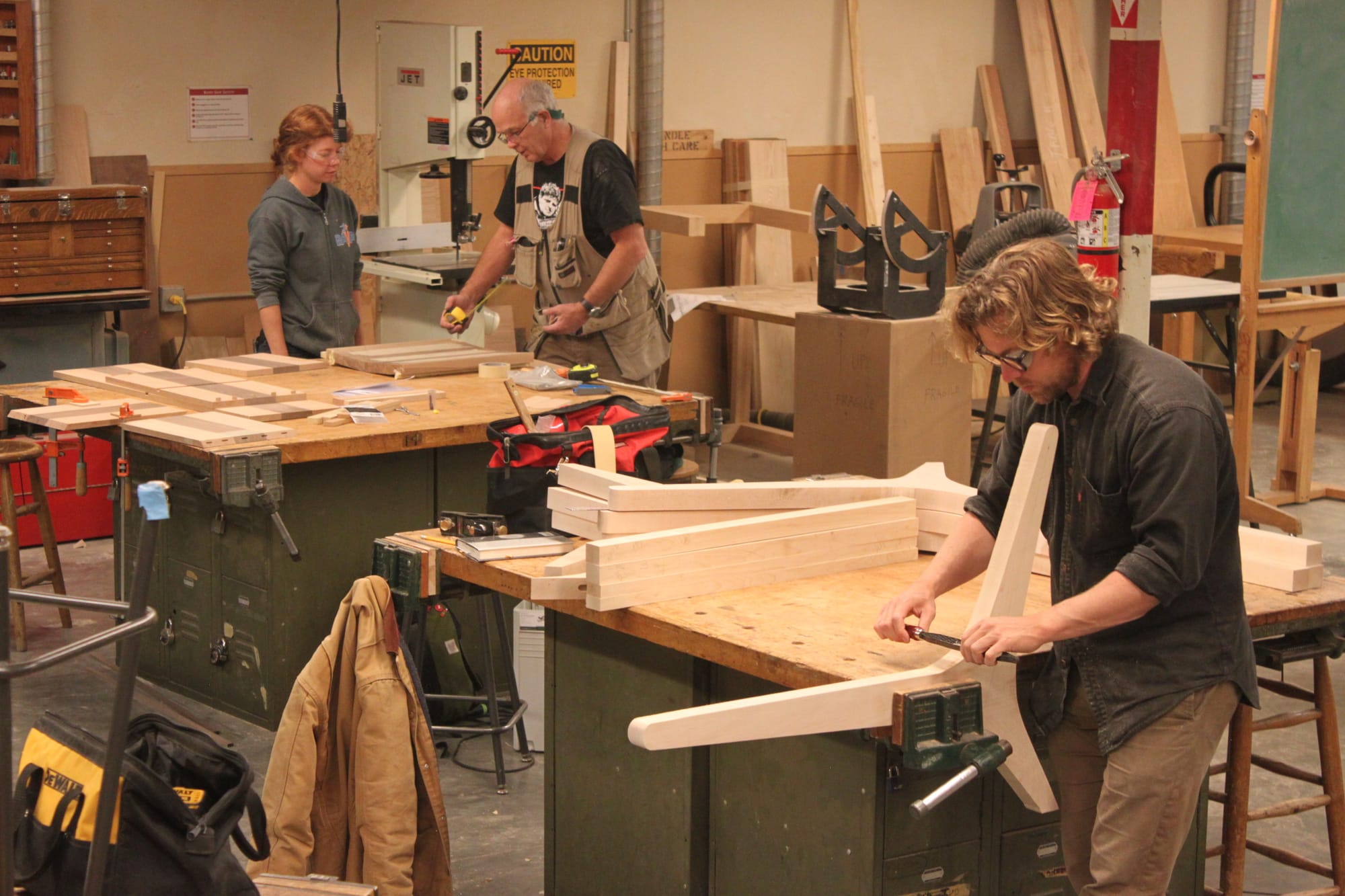 Seen working side by side are Trevor Rogers and Makenna Cook. Rogers is shaving away curls of wood on a chair he is creating out of maple, while Cook is in the background with instructor, Raymond Cash, who pulls out a tape measure. Photo taken on Oct. 27, 2017. 