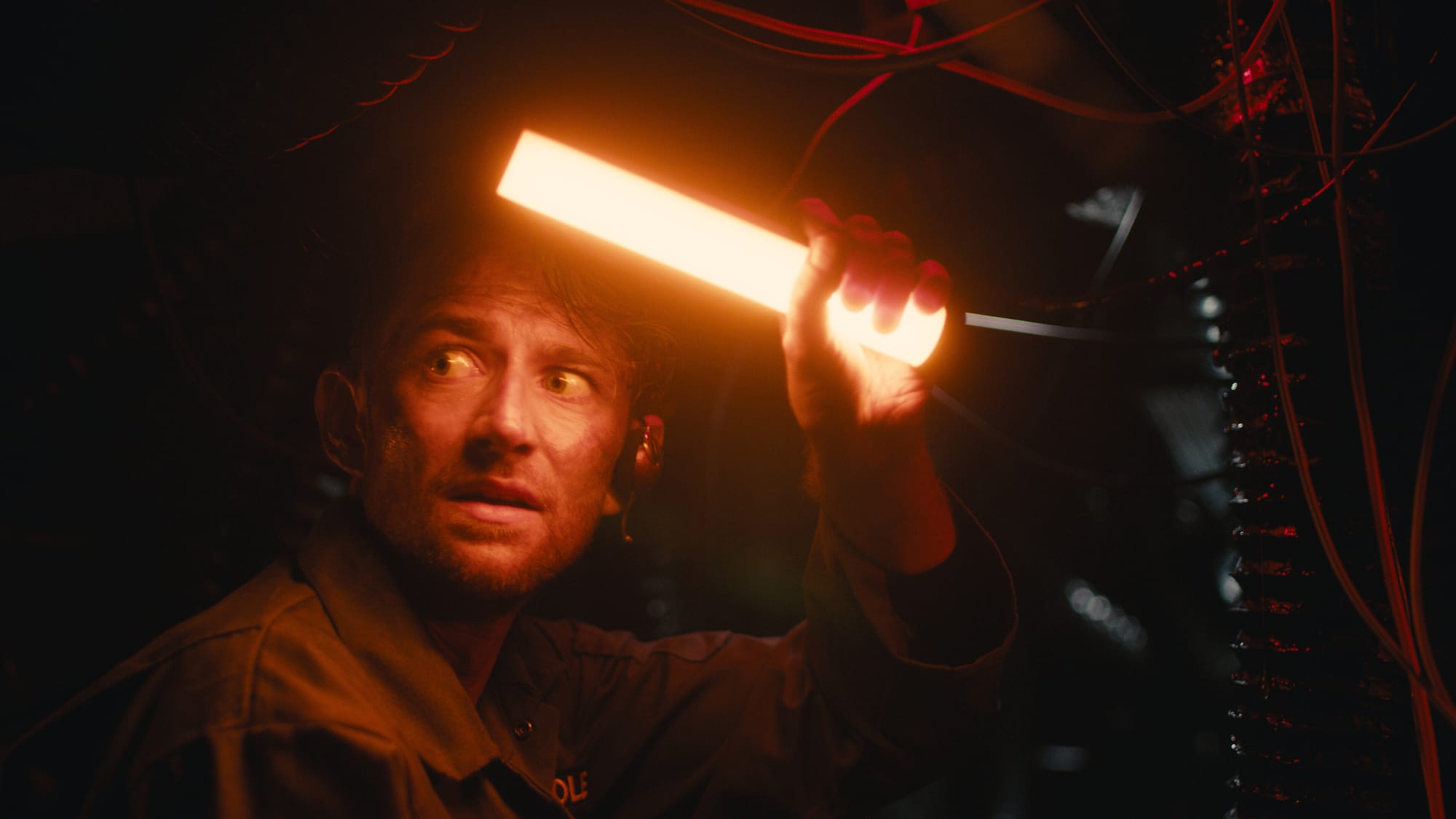 Cole Mason (Daniel Thrace) holds up a big orange glowstick while trapped in a claustrophobic corridor.