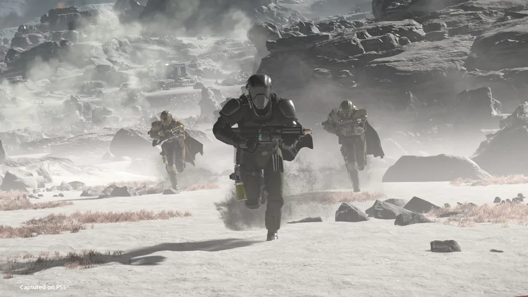 Three players run across a dusty plain on a cold tundra-esque planet in Helldivers 2.