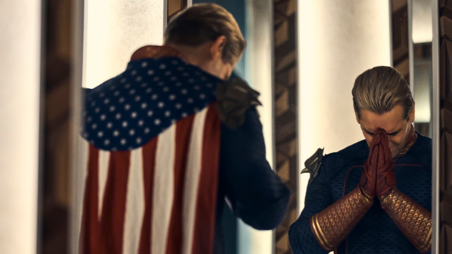 Homelander, portrayed by Antony Starr, clasps his hands together in a praying gesture and presses them against his forehead in a frustrated, pleading gesture.