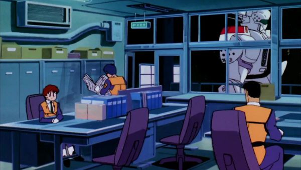 An image from the Patlabor anime, showing three characters in a mundane office sitting at chairs. In the background a Patlabor robot can be seen through the window.