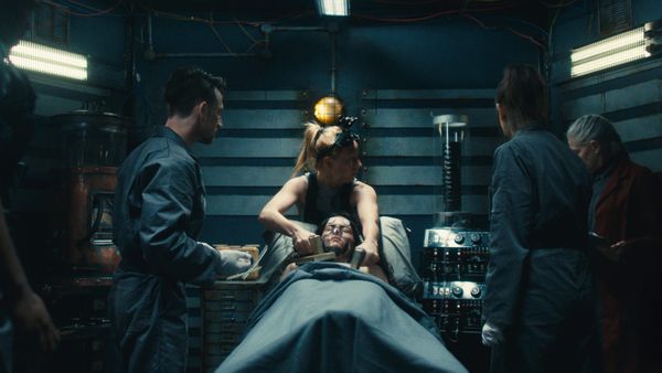  A group of people gather around a woman on a surgical table in Dead Reset, a FMV horror game set in a cramped facility with sinister secrets.