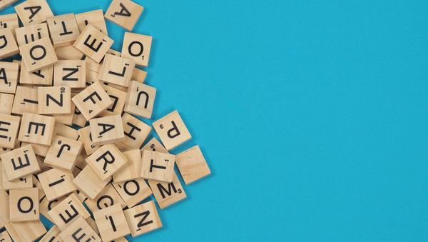 A pile of Scrabble tiles piled up against a cyan background.