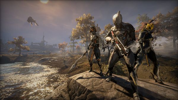 Three Warframes, high-tech space ninjas, pose with their weapons on the scenic plains of Cetus in a screenshot from Warframe.