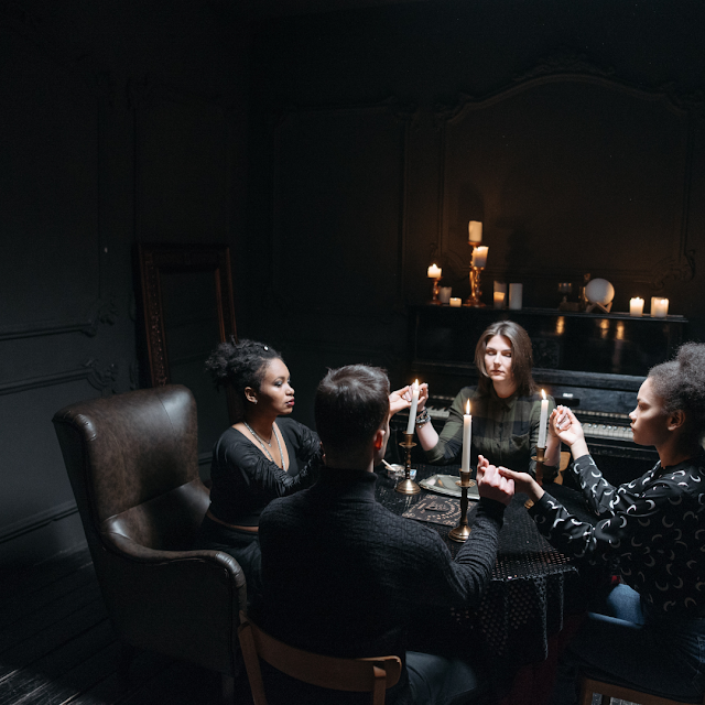 A seance with candles and people gathered around a table together. 