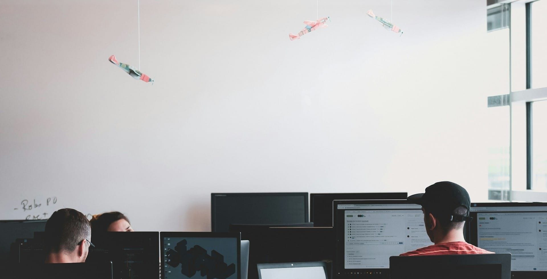 Three people on computers in conference room with whiteboard at back