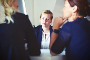 Two women interviewers in suits with their backs to the camera face a young job candidate with blones hair and blue eyes.
