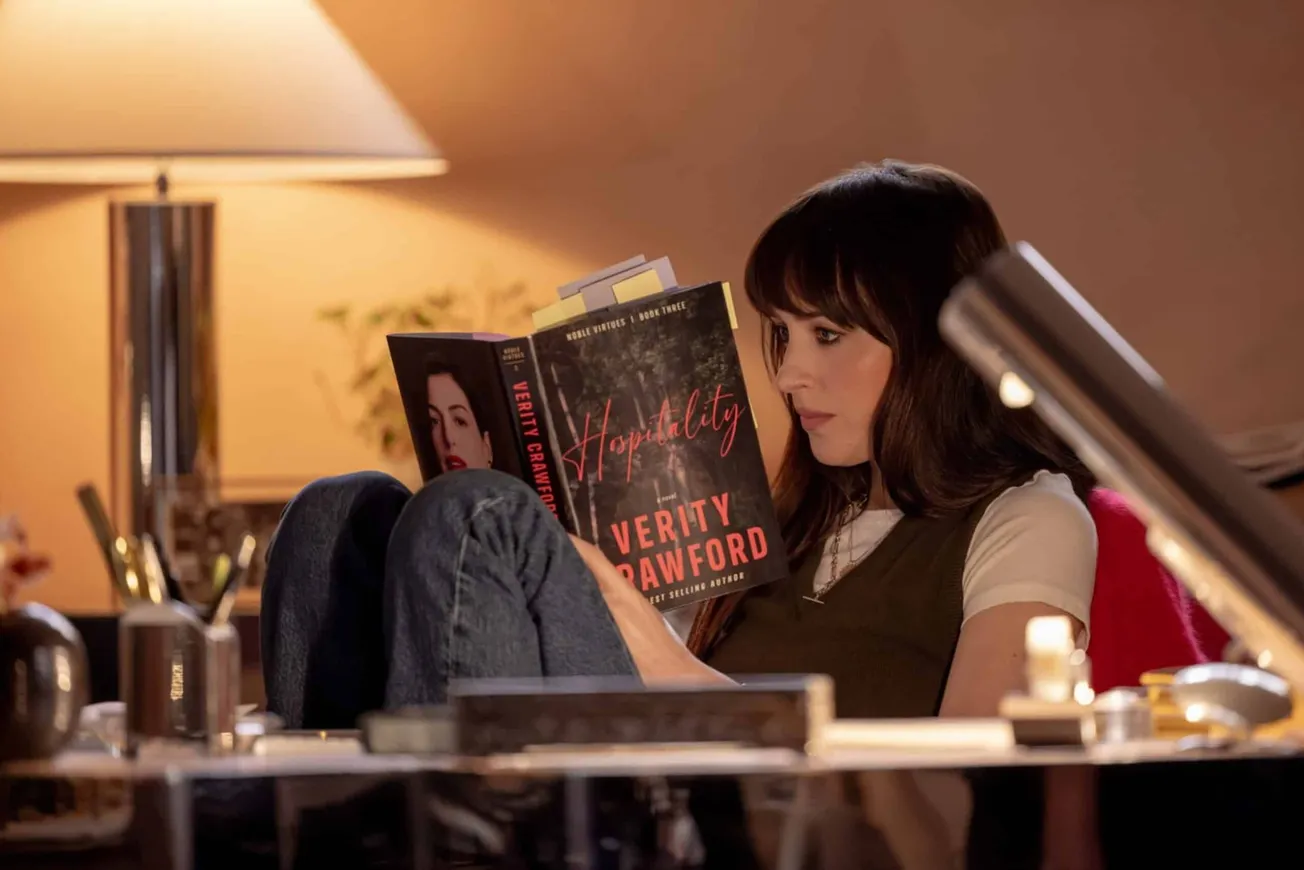 Dakota Johnson in a still from 'Verity". She is reading a book with Anne Hathaway's picture on it