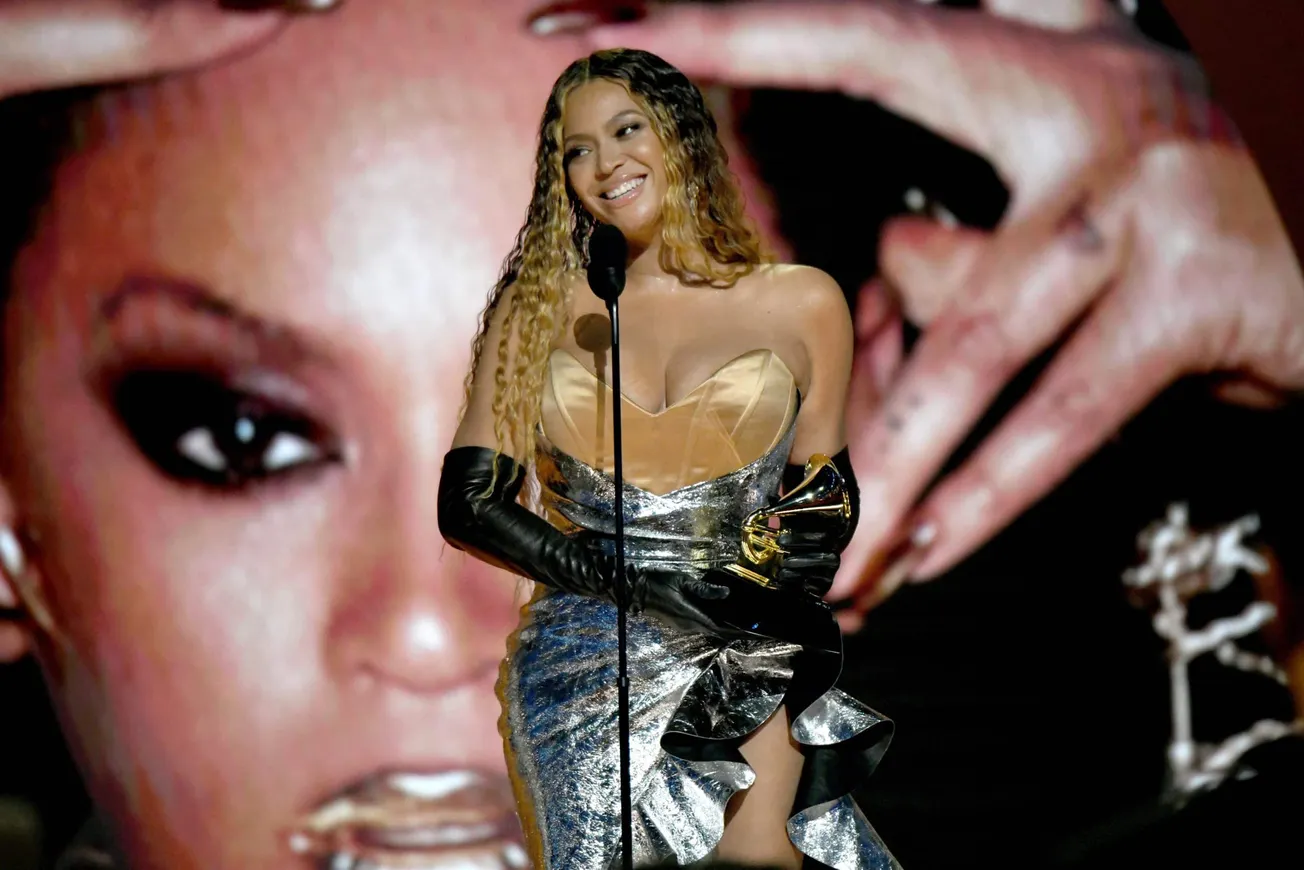 Beyoncé on stage at the GRAMMYS dressed in silver and gold and smiling.