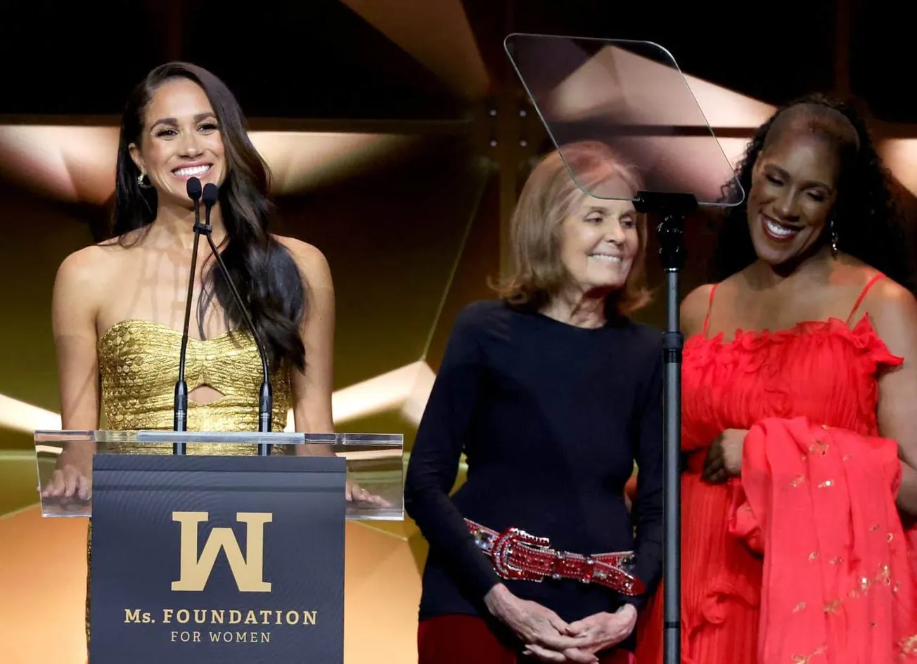 Meghan, Duchess of Sussex on stage and smiling at the Woman of Vision Awards, 2023. Beside her stand Gloria Steinem and Teres