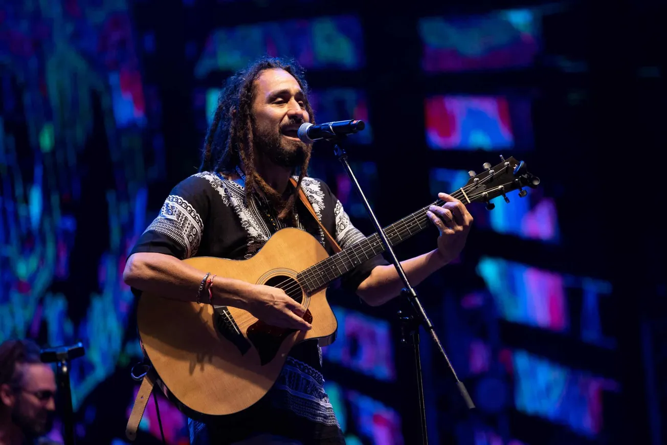 Quino McWhinney of Big Mountain performing on stage. He's holding a guitar and singing into a mic.