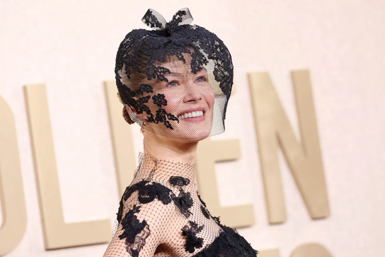 Rosamund Pike at the 2024 Golden Globe awards wearing a black lace dress with matching headpiece. She is smiling.