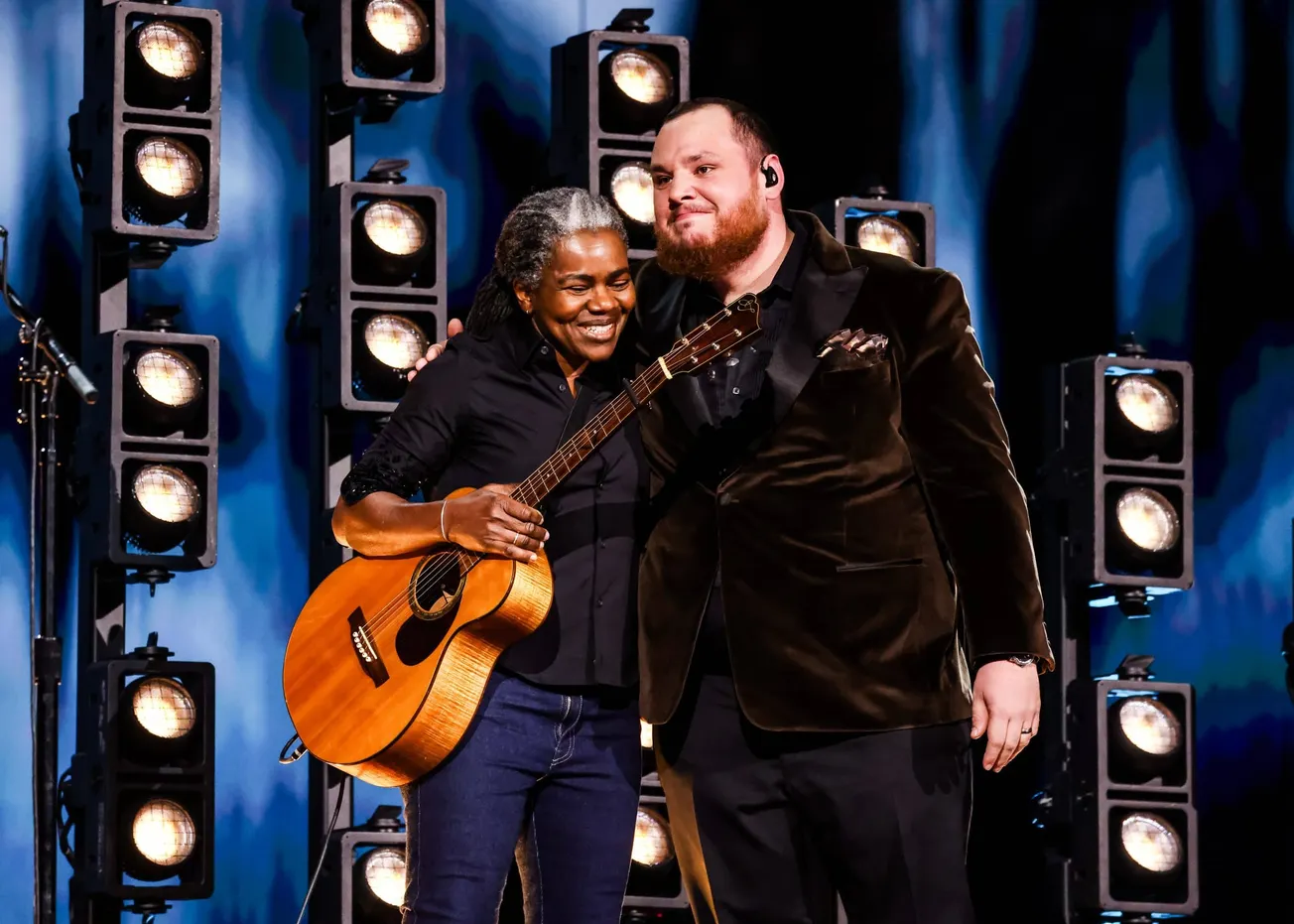 Tracy Chapman and Luke Combs hug and smile together on stage at the 2024 Grammys. Tracy is holding her guitar.