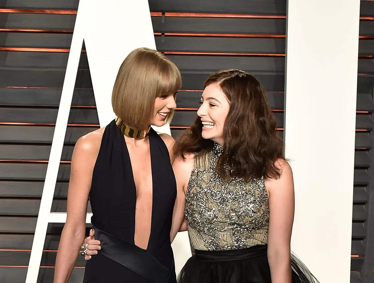 Taylor Swift and Lorde looking at each other and smiling at a red carpet event in 2016.