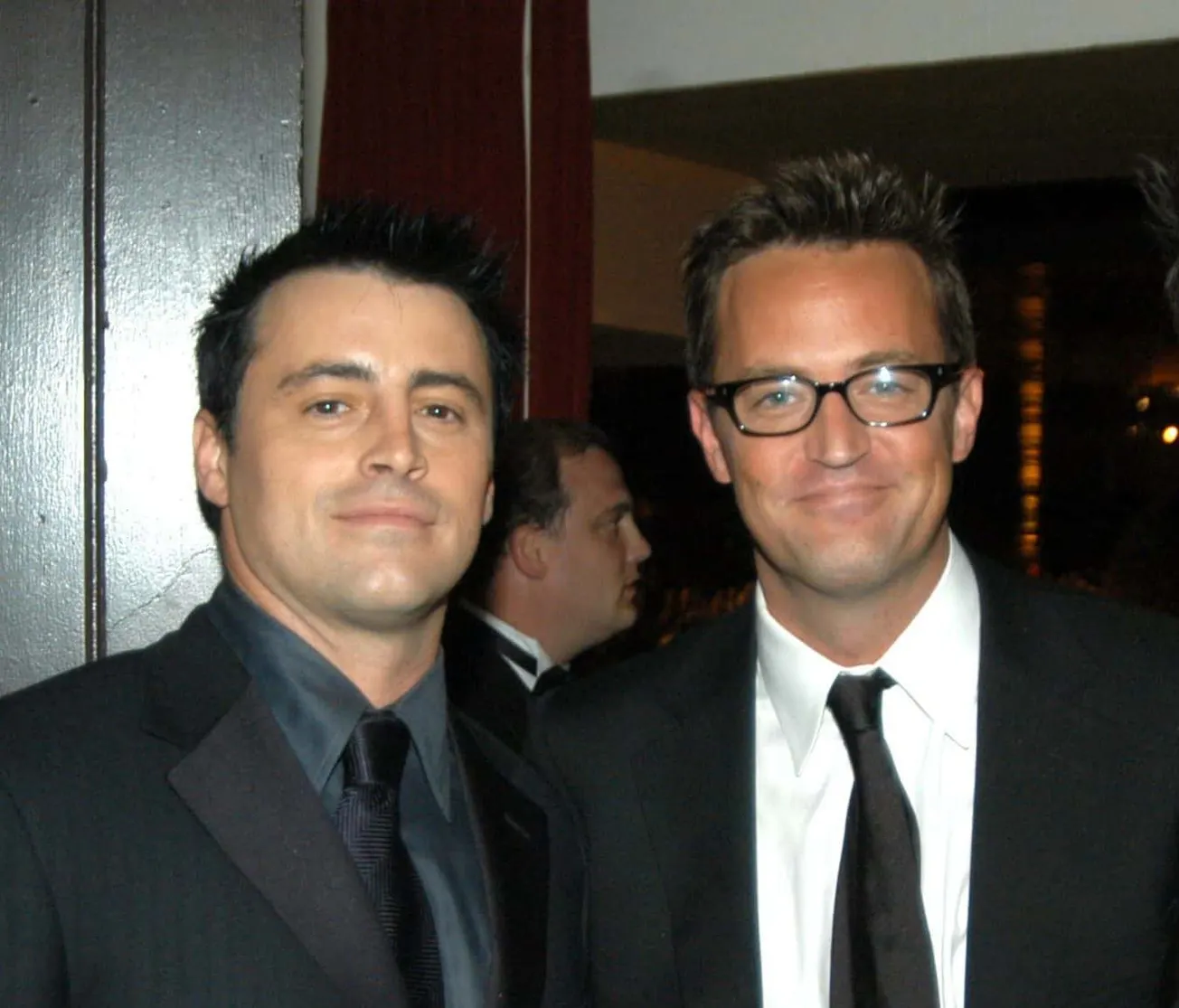 Matt LeBlanc and Matthew Perry both smiling at a press event, dressed in dark suits.