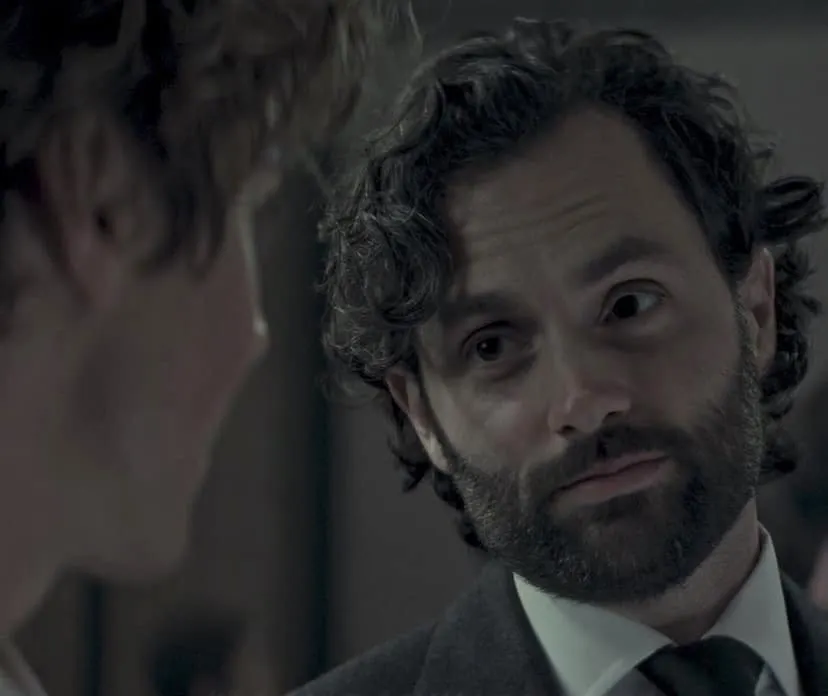a still from 'You' Netflix showing Penn Badgley as Joe Goldberg wearing a suit and looking at someone