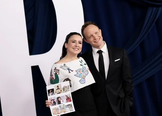 Ms. Rachel and Mr. Aron smiling together at a red carpet event. Ms. Rachel wears a dress with drawings made by kids in Gaza e