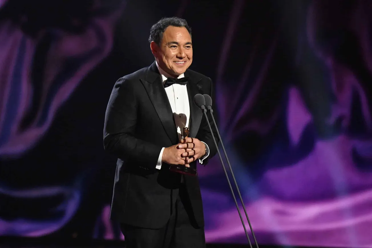 Sam Pang at the Logies speaking on stage. He wears a tux and is standing behind a mic, smiling.