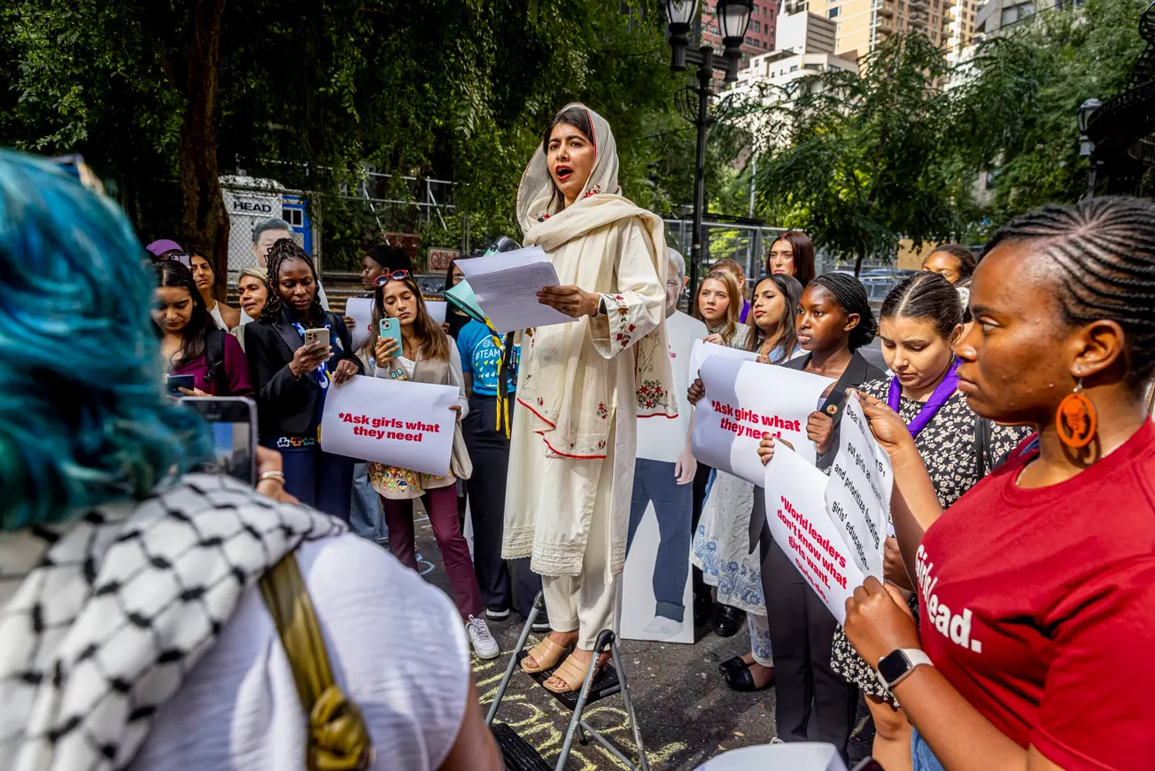 Malala Yousafzai standing on a box and speaking outside a United Nations gathering in New York City. She is surrounded by you