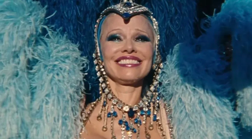 Pamela Anderson stars as Shelley in The Last Showgirl. She's dressed in a glamorous blue outfit with feathers and rhinestones