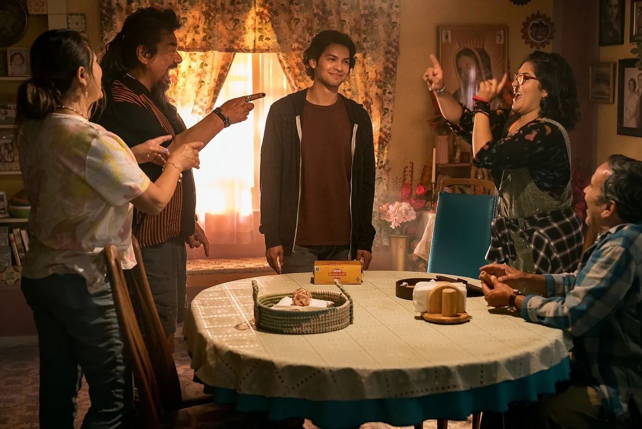 Blue Beetle cast in a still from the film. They're standing around the kitchen table pointing at Jaime Reyes.