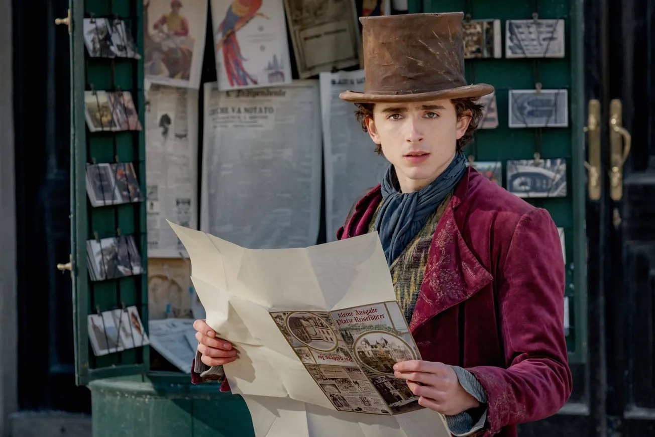 Timothée Chalamet as a young Willy Wonka holding a newspaper and looking concerned