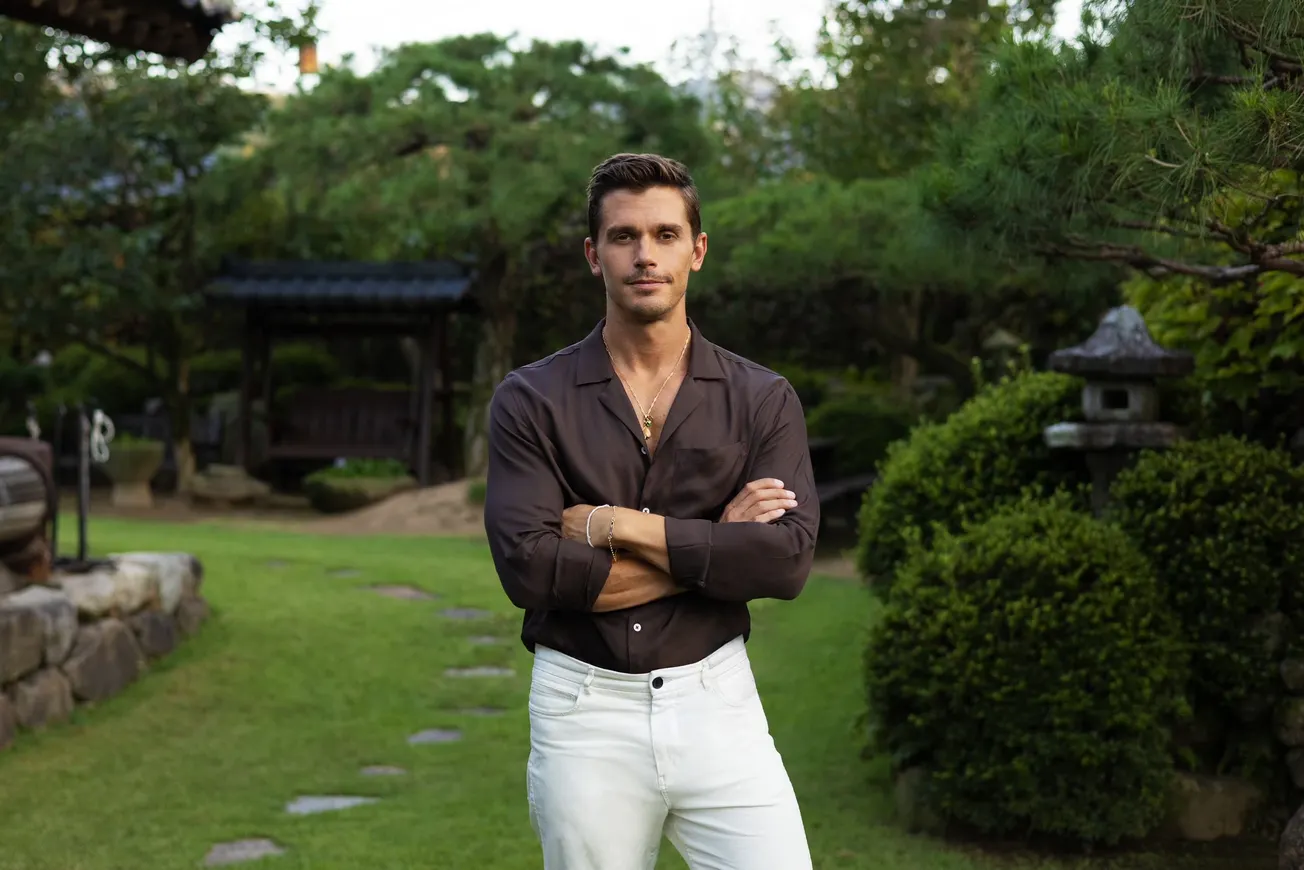 Antoni Porowski stands in an outdoor, green space with his arms crossed. This is the promo shot from Nat Geo.