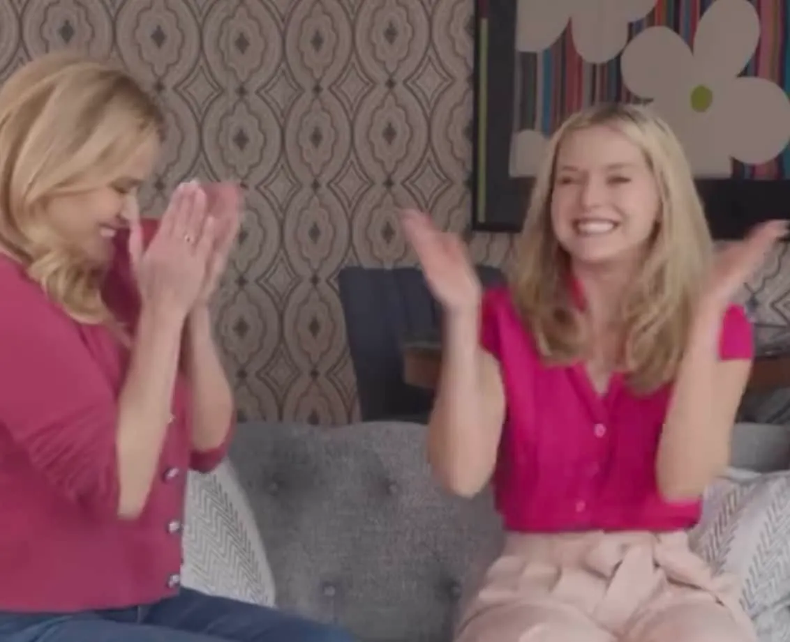 a still of Reese Witherspoon clapping as she tells Lexi Minetree she is the new Elle Woods. They are both wearing hot pink to