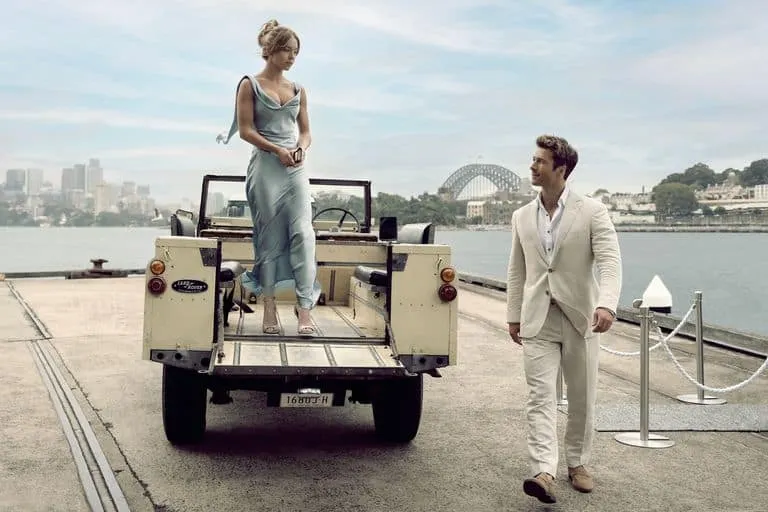 a still from Sydney Sweeney and Glen Powell's new trailer for the film 'Anyone But You'. Sydney stands on the back of an open