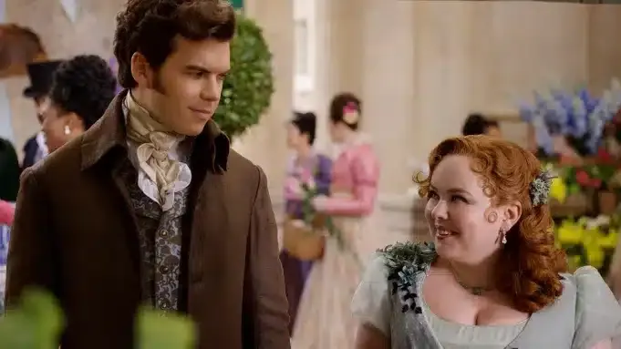 a still of Colin and Penelope from Bridgerton staring at each other and smiling, dressed in formal attire.