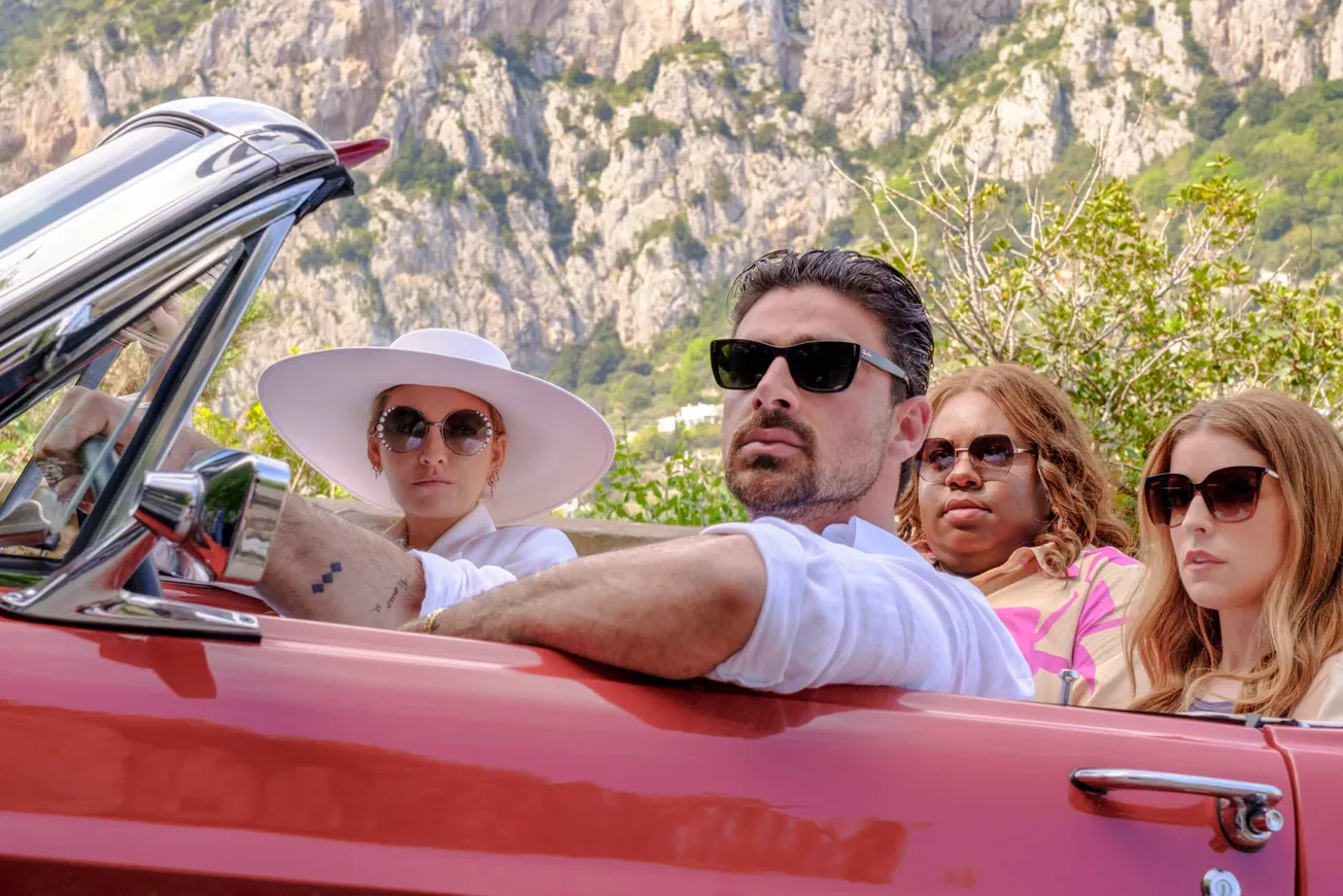 Blake Lively, Anna Kendrick, Michele Morrone and Alex Newell in a still from Another Simple Favour. They're sitting in a red