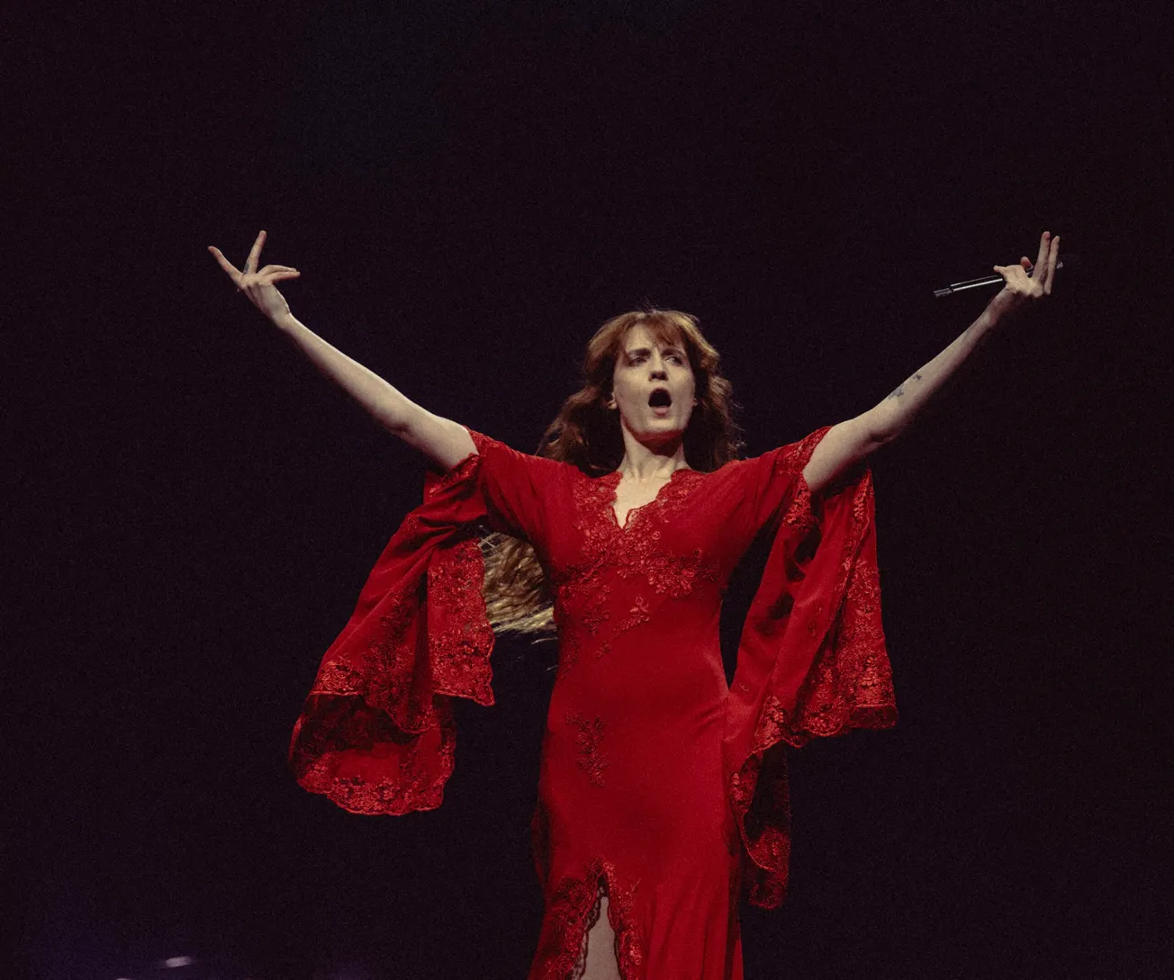 Florence Welch wears a red gwon with her arms outstretched, while performing on stage in London in February 2026
