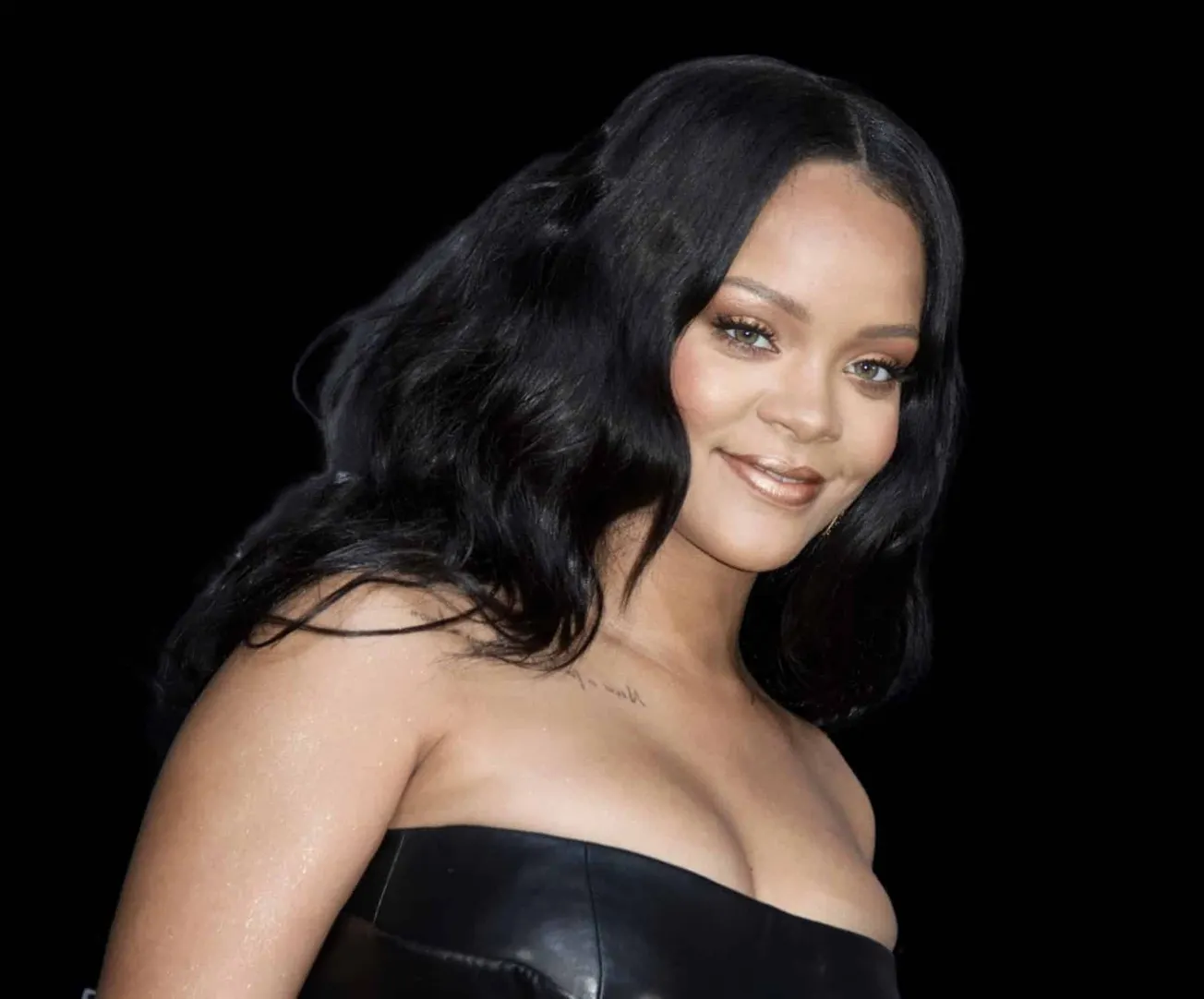 Rihanna smiles at a press event wearing a strapless black dress.