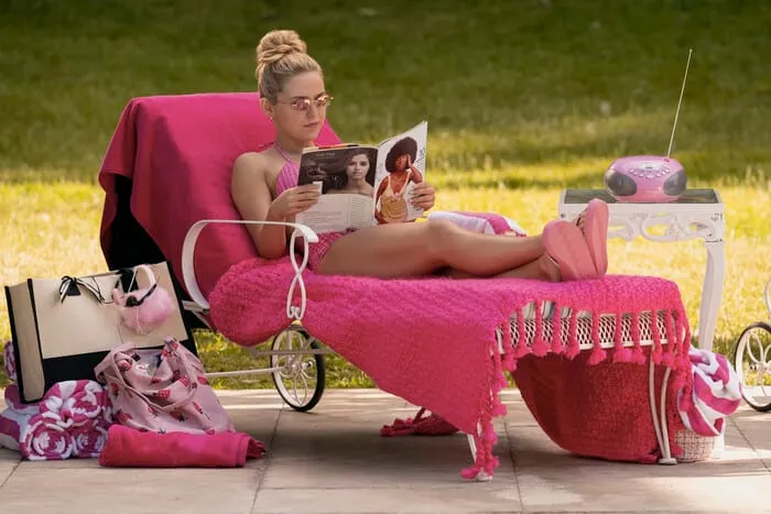 Lexi Minetree as Elle Woods in a still from 'Elle' series. She's sitting on a pink beach chair reading a magazine