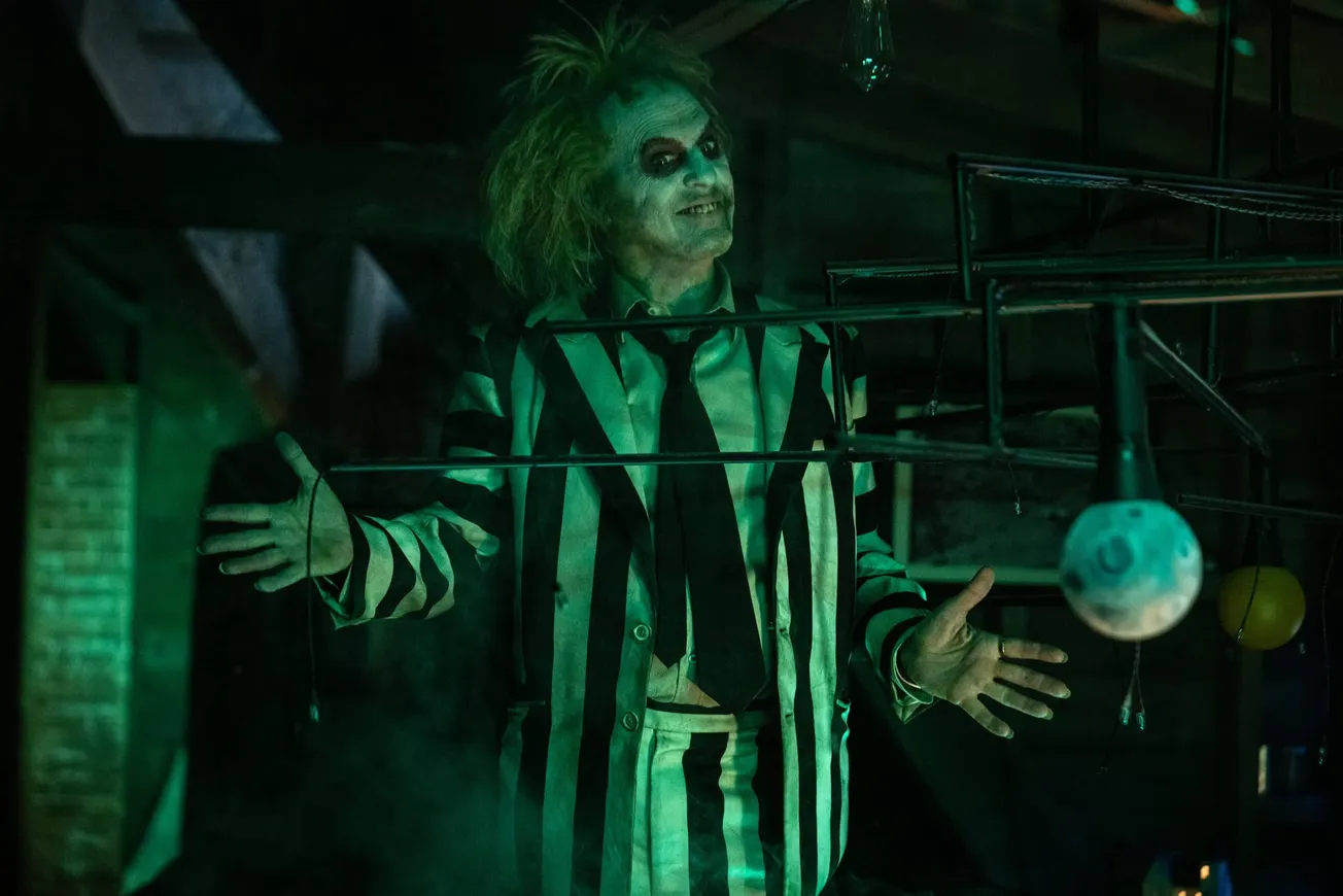 Michael Keaton reprises his role as Beetlejuice in Beetlejuice 2, wearing a striped suit and tie. His face is whitened and he