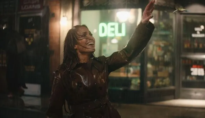 a still from Jennifer Lopez's "This is me...now: a love story" trailer showing Jennnifer smiling in the dark while it's raini