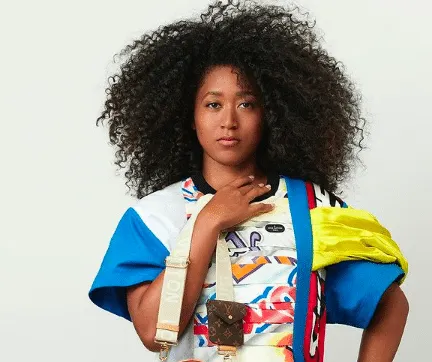 Naomi Osaka in the Louis Vuitton 2021 campaign photographed by Nicolas Ghesquière. She has an afro hairstyle, wears a bright,