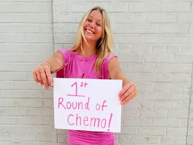 a photo of Miranda in a pink dress holding asign with pink writing that reads "1st Round of Chemo!"